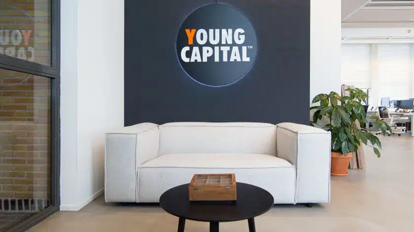Bedrijfssigning met YoungCapital logo op wand achter zithoek in modern kantoorinterieur