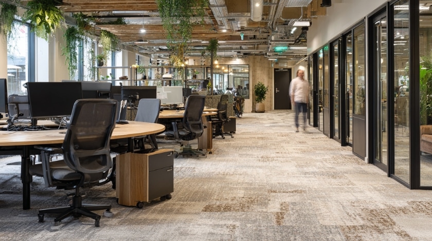 Neutrale tapijtvloer in een open kantoorruimte met werkplekken en glazen scheidingswanden, stijlvolle vloeroplossing.