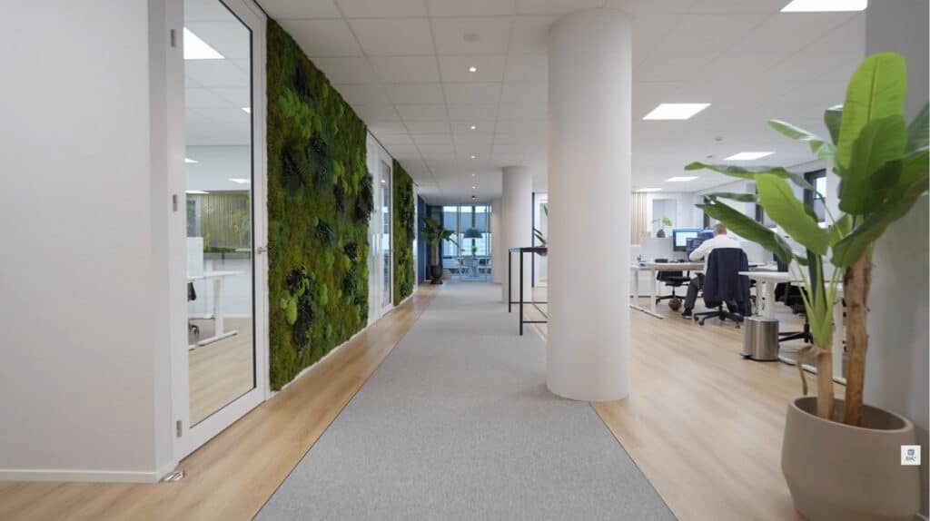 Moderne kantoorinrichting met groene moswand, houten vloer en open werkplekken, gerealiseerd door E=MC²