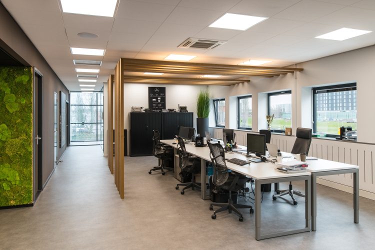 Open kantoorruimte bij Coffeeclick met moderne werkplekken, groene wand en houten details, ingericht door E=MC²